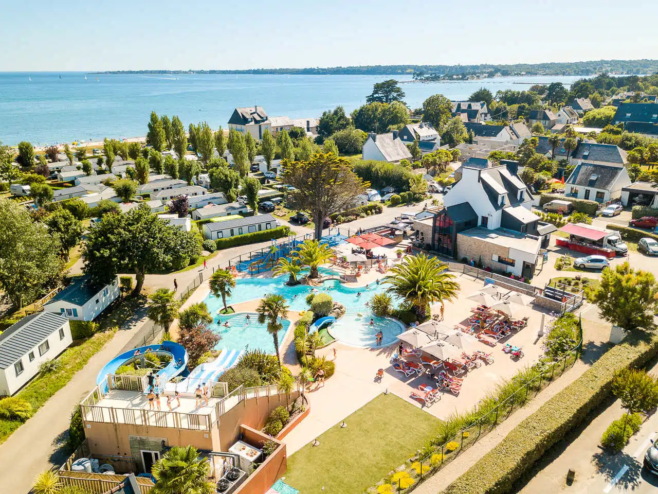Vue aérienne d'une station balnéaire du Sud, dotée de piscines, de toboggans aquatiques et d'espaces de bronzage. Nichée au milieu des arbres et des immeubles résidentiels, elle offre un mélange parfait de détente et d'aventure pour ceux qui campent dans le pittoresque Finistère.