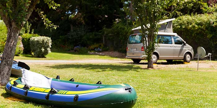 Un kayak gonflable repose sur l'herbe pr&egrave;s des arbres, capturant parfaitement le charme serein d'un emplacement de camping dans le Finist&egrave;re Sud, avec un camping-car confortable gar&eacute; &agrave; proximit&eacute;.