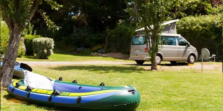 Un kayak gonflable repose sur l'espace herbeux à proximité d'un camping-car à toit ouvrant, niché au milieu des arbres et de la verdure synonymes des emplacements camping accueillants du Finistère Sud.