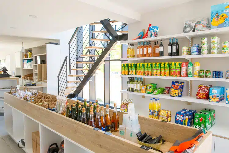 Small mini-market with shelves displaying various food, drink and snack products, ideal for shopping before your camping holiday in South Finistère. A staircase can be seen in the background.