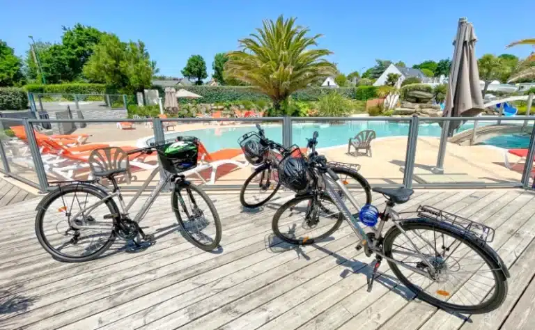Discover the serene setting of three bikes parked on a wooden terrace, with a sparkling pool and inviting poolside loungers in the background, perfect for your next adventure in beautiful Fouesnant.
