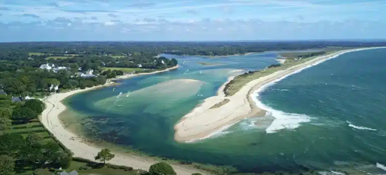 An aerial view of the coastal landscape reveals La Mer Blanche with its sandy peninsula, surrounded by verdant countryside and rhythmic ocean waves.