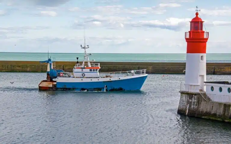 Un bateau de pêche bleu et blanc navigue près d'un phare rouge et blanc dans le charmant port du Guilvinec, une véritable pépite bretonne à découvrir.