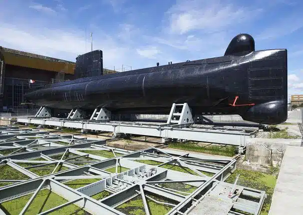 A black submarine is displayed on a shipyard platform, under a blue sky with clouds, symbolizing the innovative spirit of our collaborations.